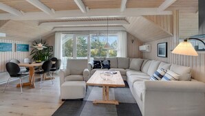 Una habitación amplia con techo de madera, un ventanal grande, un sofá, una mesa de comedor con sillas y una lámpara colgante.