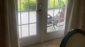 Eine Glastür führt zu einer Terrasse mit Rasen, einem grünen Stuhl und einem Fahrrad.