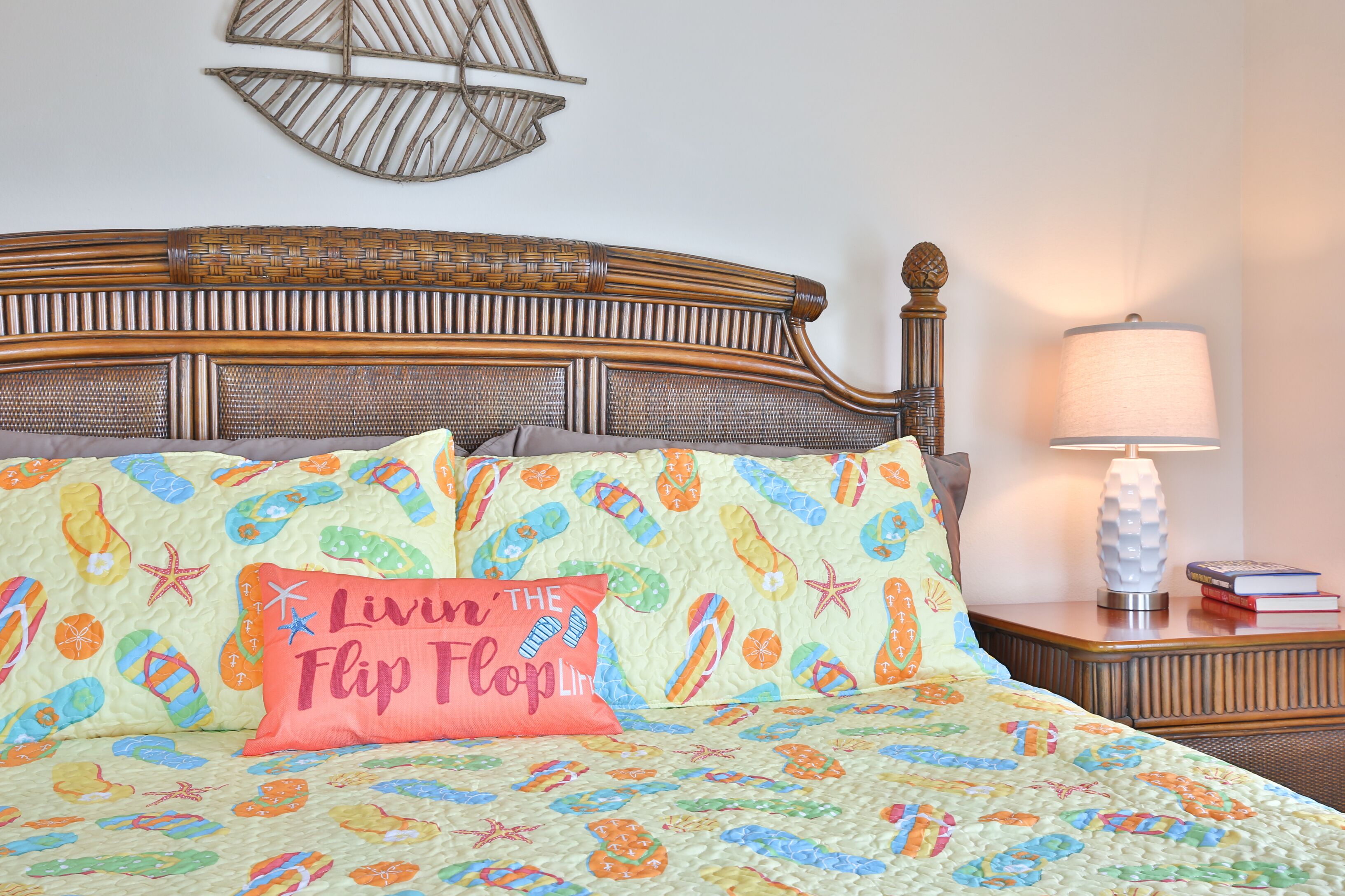 A bed with a colorful quilt featuring flip-flops and starfish, a wooden headboard, a bedside lamp, and a wall decoration.