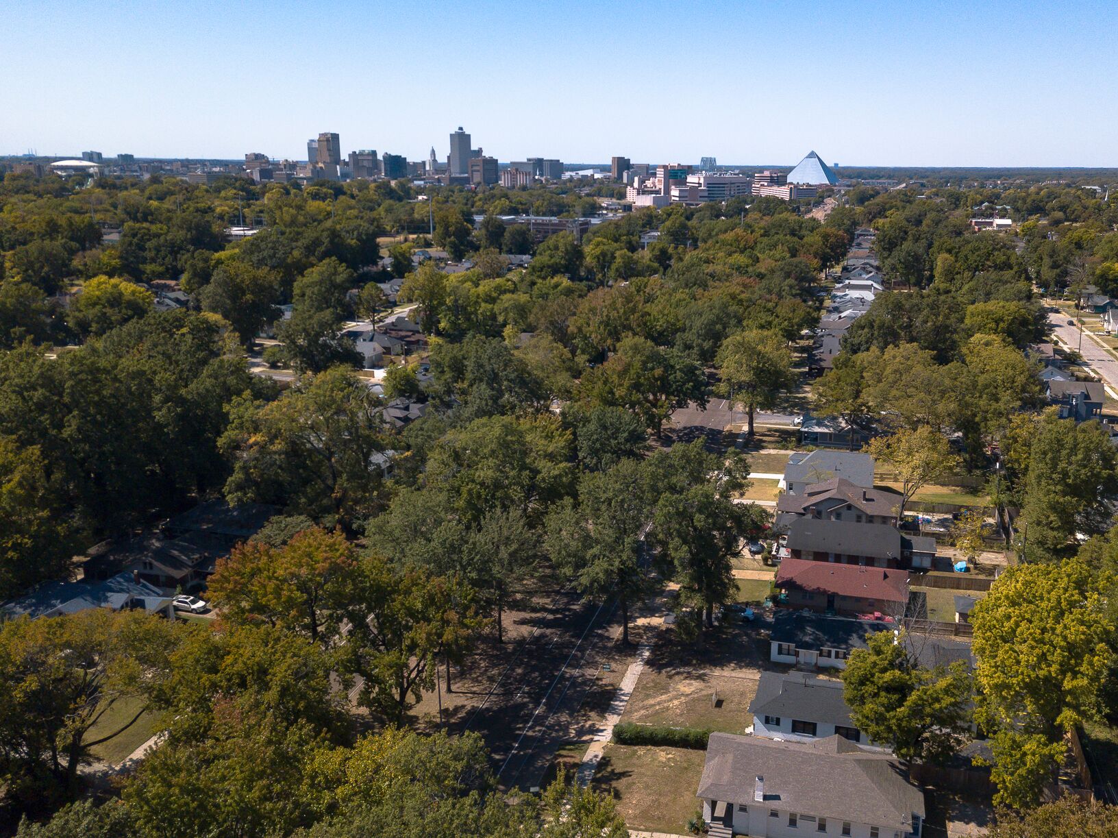 An aerial view of a residential area with houses, trees, and a distant city skyline.