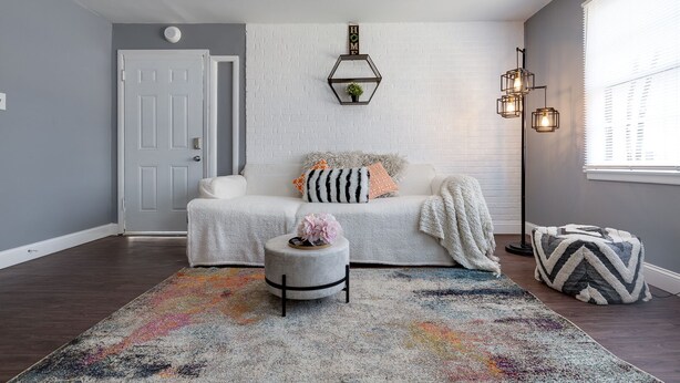 A cozy living room with a white sofa, a colorful rug, and a small round ottoman. - Medical District Gem (Memphis)