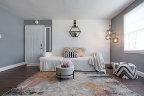 A cozy living room with a white sofa, a colorful rug, and a small round ottoman.