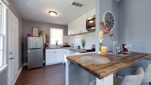 A modern kitchen with white cabinets, a wooden countertop, and a dining area with a table and chairs. - Medical District Gem (Memphis)