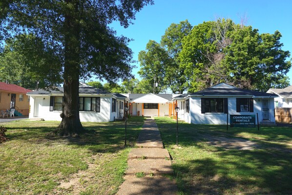 A row of single-story houses with a grassy lawn and a sidewalk leading to the entrance.