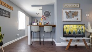 A modern kitchen with a bar area, a large clock, and a TV displaying a forest scene. - Medical District Gem (Memphis)