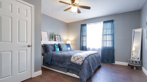 A bedroom with a bed, a ceiling fan, a window with curtains, a bedside lamp, and a mirror. - Medical District Gem (Memphis)