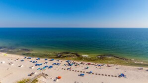 Ein Strand mit vielen Sonnenschirmen und Liegestühlen, einem klaren Himmel und ruhigem Meer.