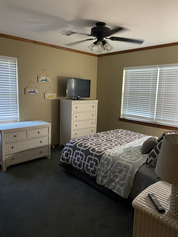 A bedroom with a bed, dresser, TV, and ceiling fan.
