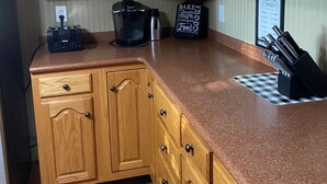 Une cuisine avec des meubles de rangement en bois, un plan de travail, une machine à café, une bouilloire et un bloc à couteaux.