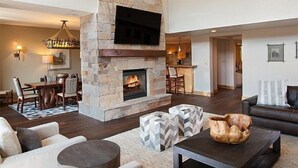 Un salón amplio con chimenea de piedra, muebles modernos y una cocina al fondo.
