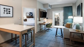 Una habitación de hotel con cama, escritorio, silla, televisor, mesa y sofá.