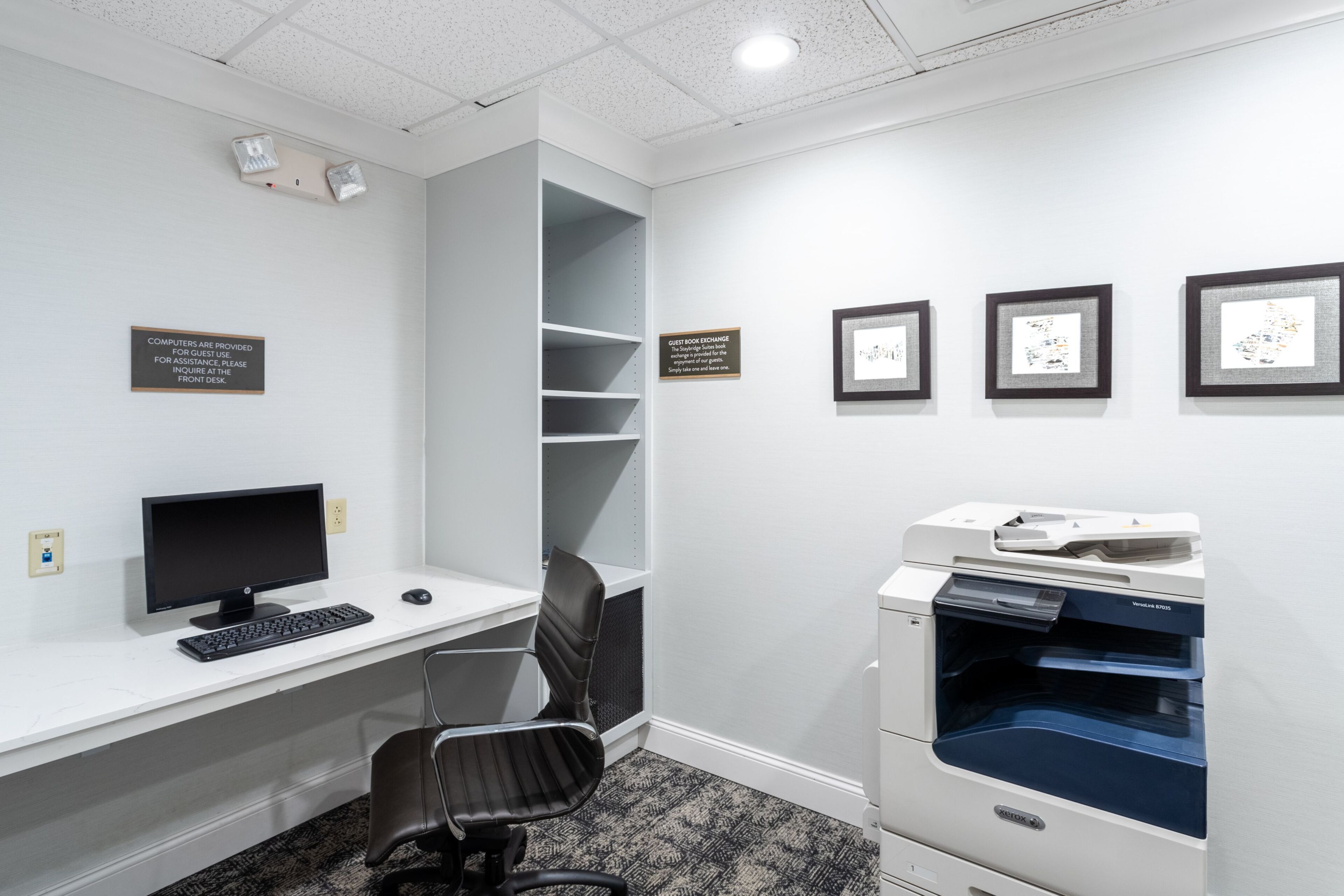 A modern office space with a desk, computer, chair, printer, and framed artwork on the wall.