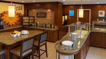 A hotel breakfast area with a stone wall, a sign for free daily breakfast, and a buffet counter with various food items.