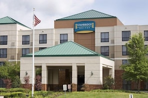 Um hotel Staybridge Suites com telhado verde, um mastro com a bandeira americana e uma placa indicando o nome do hotel.