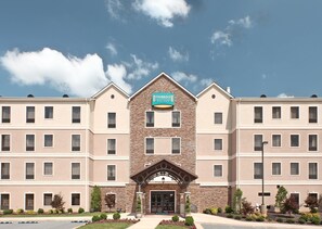 Ein mehrstöckiges Hotel mit einer steinernen Fassade, einem zentralen Eingang und einem Schild mit der Aufschrift "Staybridge Suites".