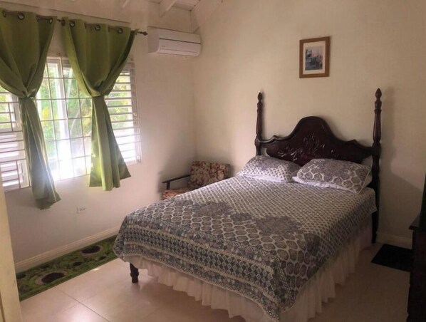 Un dormitorio con cama, cortinas, un aire acondicionado y una mesita con silla.