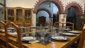 A dining room with a large wooden table set for six, surrounded by wooden chairs.