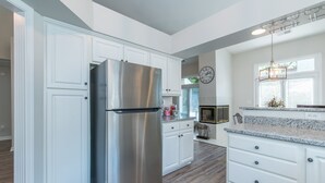 Una cocina moderna con armarios blancos, un refrigerador de acero inoxidable, encimeras de granito y una lámpara colgante.