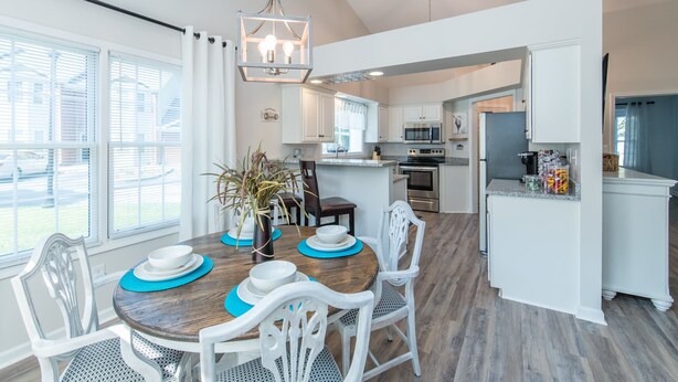 Una cocina moderna con armarios blancos, una isla central y un comedor con mesa de madera y sillas blancas.