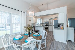 A modern kitchen with white cabinets, a central island, and a dining area with a wooden table and white chairs. - Southern Charm - 2BR - BBQ - Walk to Kroger Field (Lexington)