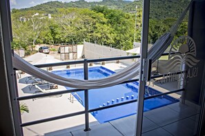 A view of a swimming pool from a balcony with a hammock, surrounded by greenery and a mountainous landscape. - Isla Bonita Hotel (Zihuatanejo)
