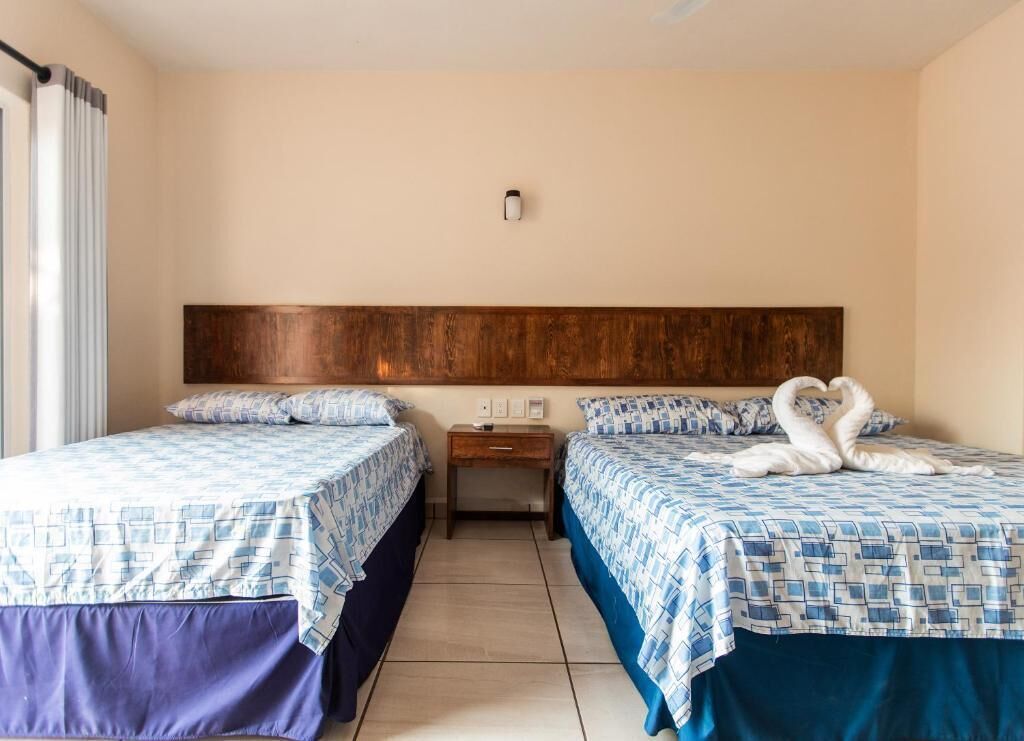 A hotel room with two beds, a wooden headboard, a nightstand, and a wall-mounted light.