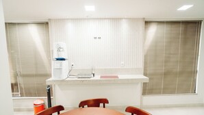 A small, clean room with a table and chairs, a water dispenser, and a window with blinds. - Hotel Albinos (Itaperuna)
