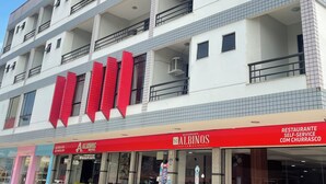 A multi-story hotel with balconies, a red awning, and a sign indicating a restaurant with self-service churros. - Hotel Albinos (Itaperuna)