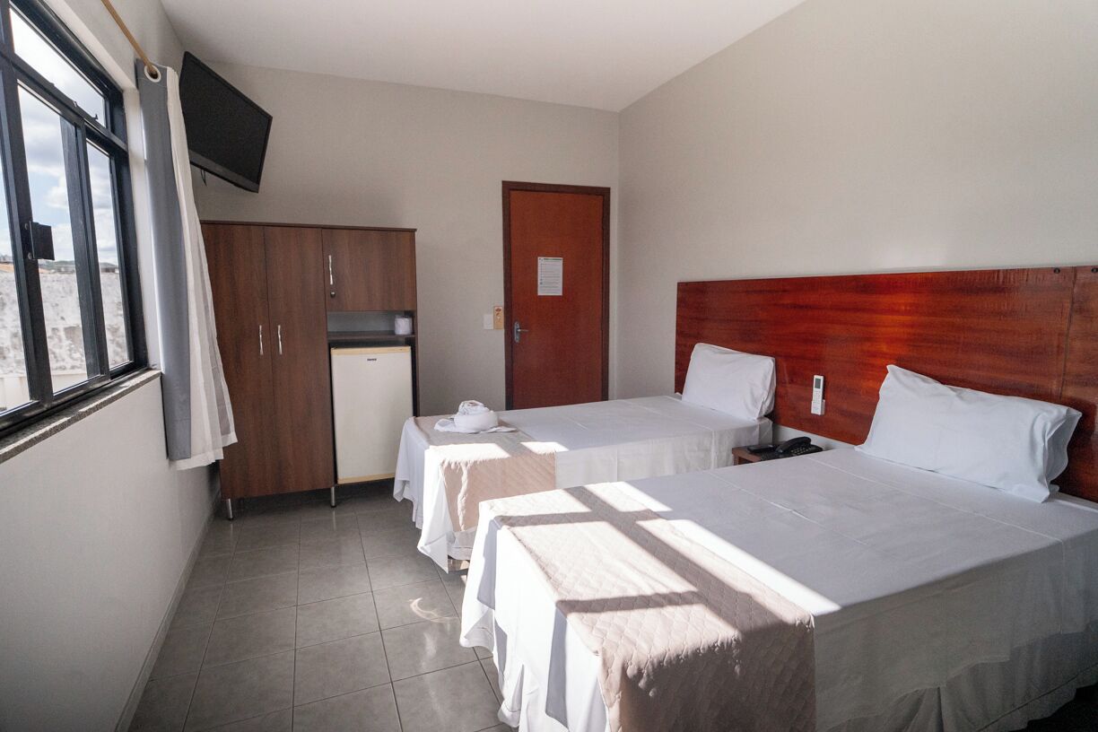 A hotel room with two beds, a wooden wardrobe, a television, and a window with curtains.