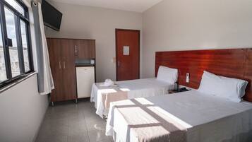 A hotel room with two beds, a wooden wardrobe, a television, and a window with curtains.