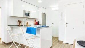 Een compacte keuken met een magnetron, koffiezetapparaat en een klein eiland met stoelen.