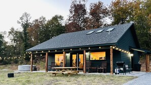 A rustic cabin with a covered porch, string lights, and outdoor seating. - Modern Cabin w/Pool and Hot Tub! (Mountain View)