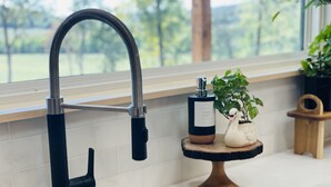 A kitchen with a modern faucet, a small wooden table with a soap dispenser and a swan decoration, and a stainless steel sink. - Modern Cabin w/Pool and Hot Tub! (Mountain View)