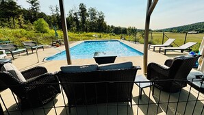 A covered outdoor area with a swimming pool, wicker furniture, and a view of the countryside. - Modern Cabin w/Pool and Hot Tub! (Mountain View)