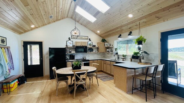 A modern kitchen with wooden ceiling beams, a central island, and a dining area with chairs. - Modern Cabin w/Pool and Hot Tub! (Mountain View)