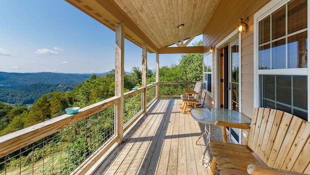 A wooden deck with a glass table and chairs, overlooking a forested valley. - Three-Level Cabin with Mountain Views (Boone)