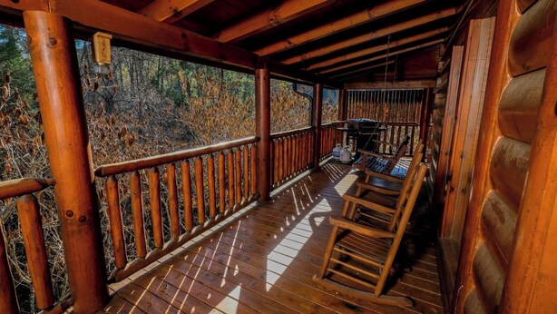 Una terrassa de fusta amb barana, una cadira d'oscil·lació i vista a un bosc.