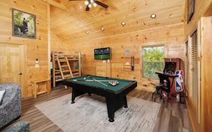 A wooden interior with a pool table, a television, and an arcade machine.