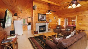 Een gezellig interieur van een chalet met een open haard, leren banken, een eethoek en een keuken.