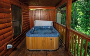 Un jacuzzi en una cabaña de madera con una terraza de madera y vistas al bosque.