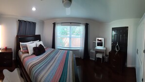 A bedroom with a bed, bedside table, dresser, vanity, and a window with curtains.