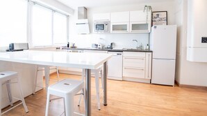 Moderni keittiö, jossa on valkoiset kaapit, keskellä oleva saareke jakkaroineen sekä sisäänrakennettu uuni, mikroaaltouuni ja astianpesukone.