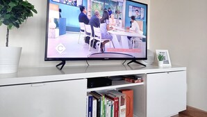 Televisiossa näkyy kohtaus, jossa huoneessa on ihmisiä, ruukussa oleva kasvi ja kirjahylly täynnä kirjoja.
