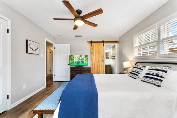 A bedroom with a bed, a ceiling fan, a TV, a wooden door, and a window with blinds.