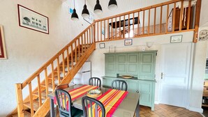 A dining area with a wooden staircase, a green kitchen, and a white door.