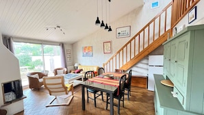 A cozy living room with a wooden staircase, a dining table with chairs, and a kitchen area with cabinets.