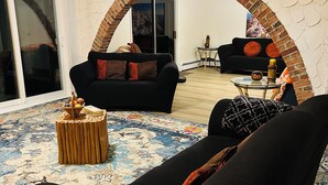 Una sala de estar con un sofá negro, un tapete estampado, una mesita de madera y un arco de ladrillo que da a un balcón.