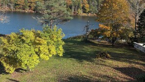 Vista panorámica de un lago rodeado de árboles en tonos otoñales, con un área verde y cielo despejado.