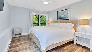 Ein Schlafzimmer mit Bett, Nachttischlampen, Deckenventilator, Fenster mit Aussicht und einer Wand-Klimaanlage.