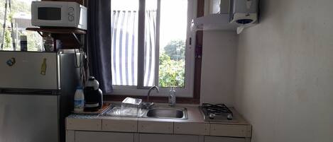 A compact kitchen with a refrigerator, microwave, sink, and gas stove.